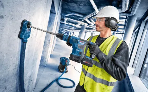 Operaio con trapano a percussione e punte trapano per cemento armato, pronto a forare un muro in cantiere.