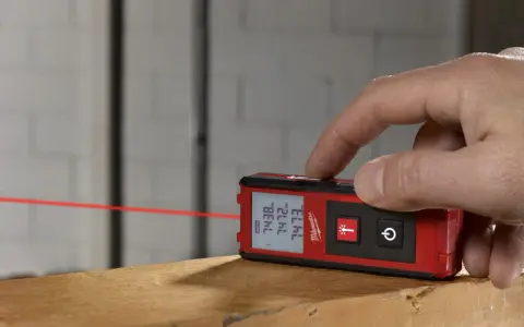 Dito come si usa il metro laser Milwaukee per misurazioni precise. Un dito preme il pulsante per attivare il raggio laser rosso.