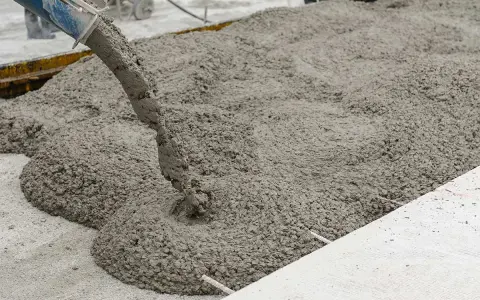 Il cemento fresco viene versato da una betoniera, mostrando come si fa il cemento per una nuova pavimentazione.