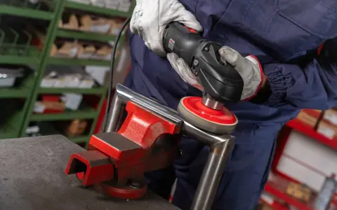 Operaio usa una lucidatrice con dischi abrasivi, parte dei prodotti per lucidare l'acciaio, per rifinire un pezzo metallico fissato in una morsa.