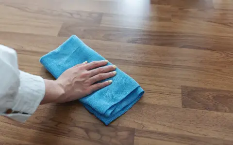 Mano con panno blu pulisce superficie in legno, mostrando come togliere la colla dal legno con delicatezza.
