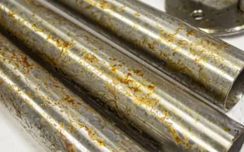 Tre tubi metallici mostrano segni di ruggine e corrosione, con l'acciaio annerisce in alcune aree.