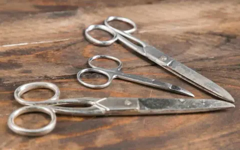 Tre forbici di metallo su un tavolo di legno. Scopri come togliere la ruggine dalle forbici per farle tornare come nuove.