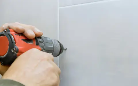 Mani che usano un trapano per fare un buco nel muro bianco.