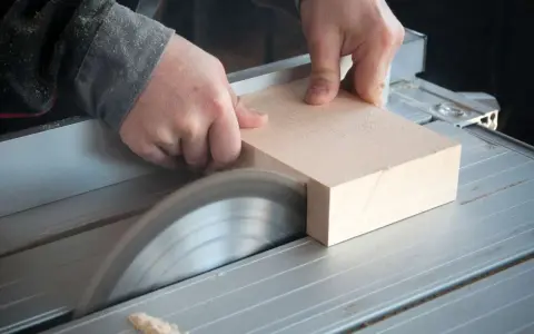 Mani esperte guidano un pezzo di legno su una sega circolare per tagliare legno a mano con precisione.