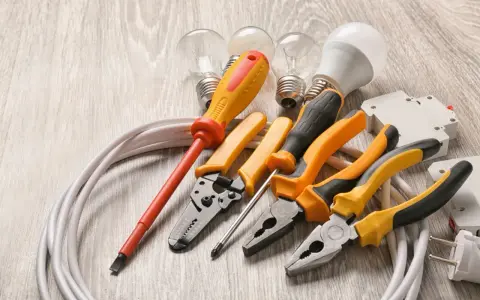 Un set di strumenti per elettricisti: pinze, cacciaviti, lampadine e cavi su un tavolo di legno.