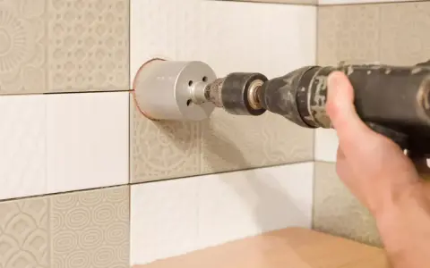 Mano che usa una sega a tazza per forare piastrelle per tubi.