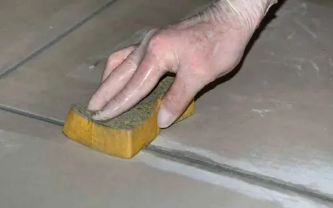 Mano con guanto in lattice che rifinisce le fughe dei pavimenti con una spugna umida.