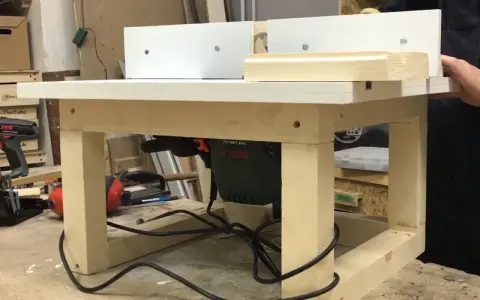 Banco fresa fai da te con fresatrice Bosch montata sotto il piano di lavoro. Un pezzo di legno viene lavorato.