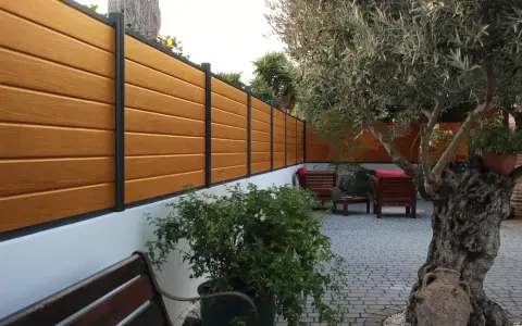 Pannello in legno effetto teak fissato a un muro bianco, con un ulivo secolare e arredi da esterno. Ideale per capire come fissare un pannello di legno al muro.