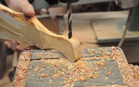 Mano che trapana un pezzo di legno grezzo, creando un tagliere legno fai da te. Segatura ovunque.