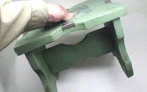 Mano che tiene uno sgabello di legno verde, pronto per verniciare con bomboletta spray.