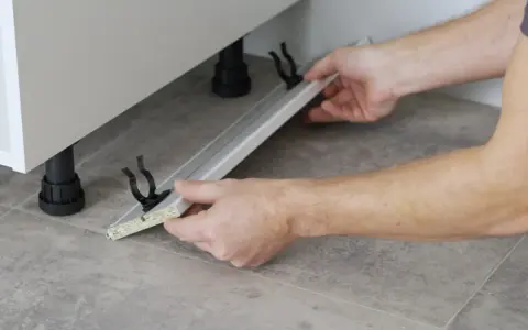 Mani che assemblano uno zoccolo cucina in alluminio, mostrando come tagliare e fissare i supporti.