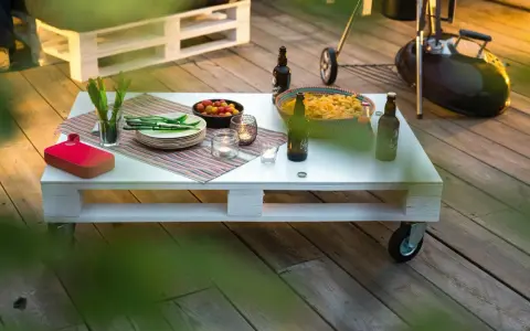 Tavolo con pallet fai da te, pronto per un barbecue con birre, patatine e pomodorini.
