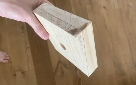 Mano che tiene un pezzo di legno con segni di matita, come se si stesse pensando a come tagliare il legno senza attrezzi.