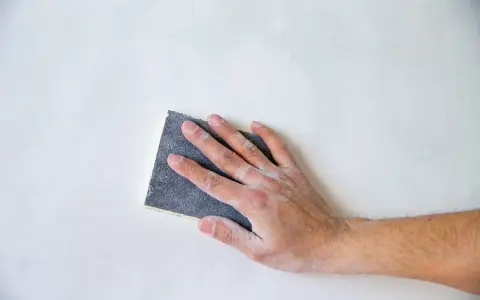 Mano che leviga una superficie bianca con carta vetrata per legno, quale usare per un lavoro perfetto.