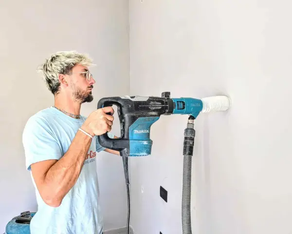 Giovane con capelli biondi usa un trapano Makita per fare un foro nel muro. Il trapano non buca muro, ma aspira la polvere.
