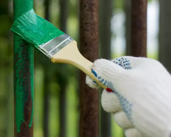 Mano guantata che vernicia di verde un palo di metallo arrugginito, rinnovando la verniciatura.