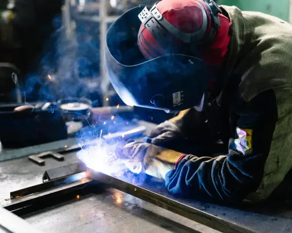 Saldatore al lavoro, scintille luminose e fumo blu avvolgono la tempra dell'acciaio inox.