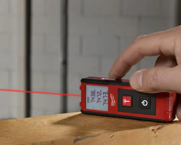 Dito come si usa il metro laser Milwaukee per misurazioni precise. Un dito preme il pulsante per attivare il raggio laser rosso.