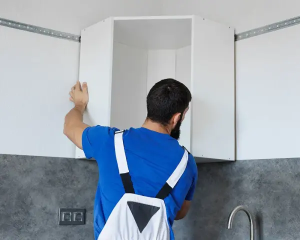 Installazione di pensili da cucina: un uomo con tuta blu monta un pensile angolare su una guida a muro.