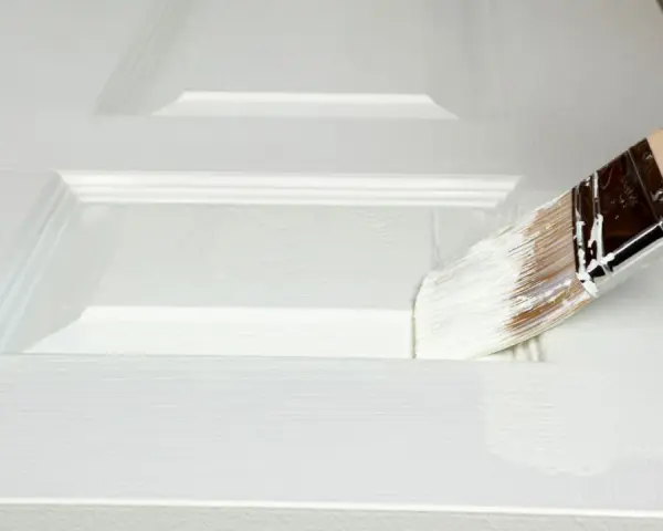 Pennello bianco applica vernice su porta in legno già verniciata, mostrando come verniciare una porta in legno già verniciata.