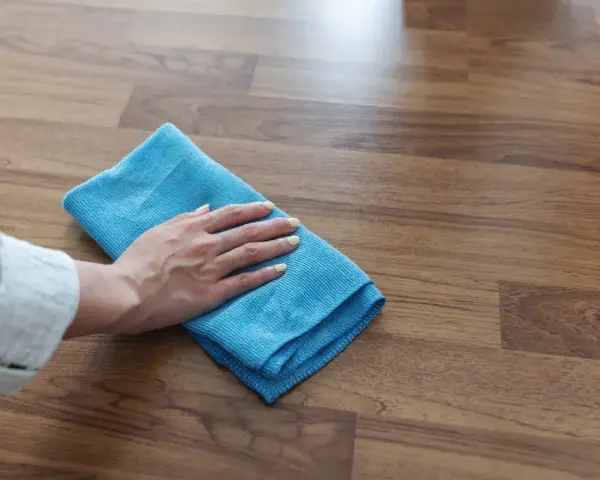 Mano con panno blu pulisce superficie in legno, mostrando come togliere la colla dal legno con delicatezza.