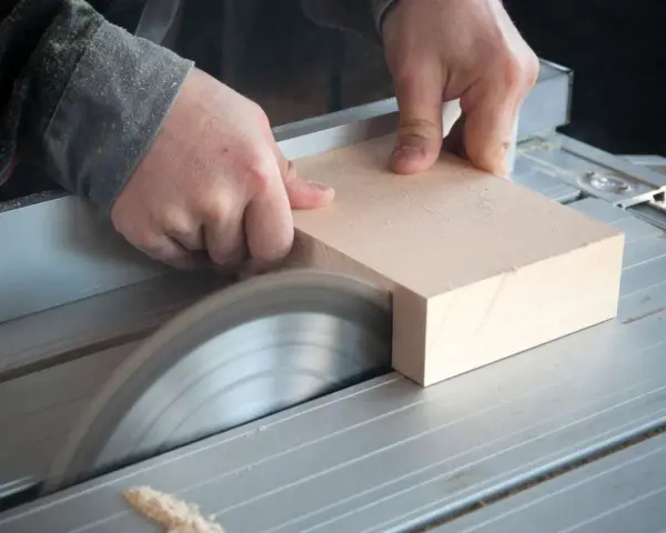 Mani esperte guidano un pezzo di legno su una sega circolare per tagliare legno a mano con precisione.