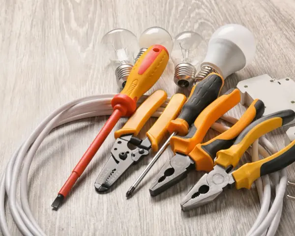 Un set di strumenti per elettricisti: pinze, cacciaviti, lampadine e cavi su un tavolo di legno.
