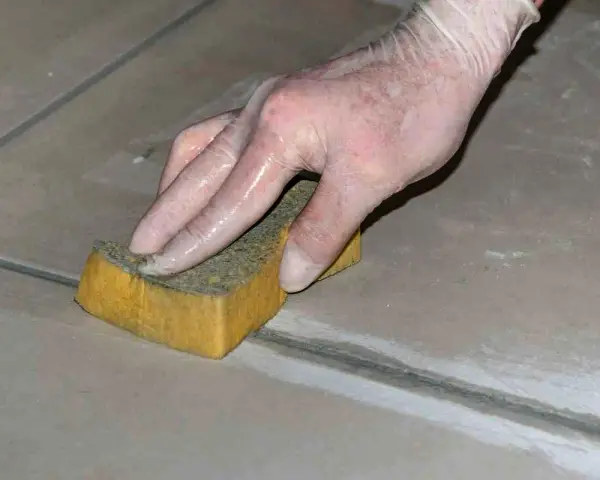 Mano con guanto in lattice che rifinisce le fughe dei pavimenti con una spugna umida.