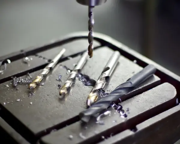 Trapano a colonna: componenti pronti per il lavoro. Diverse punte da trapano, alcune usate, giacciono sulla tavola di lavoro, circondate da trucioli metallici.