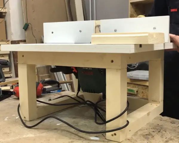 Banco fresa fai da te con fresatrice Bosch montata sotto il piano di lavoro. Un pezzo di legno viene lavorato.