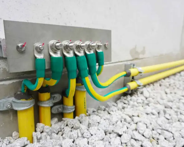 Cavi verdi e gialli collegati a una barra di messa a terra su una parete di cemento, con tubi gialli che escono dal terreno.