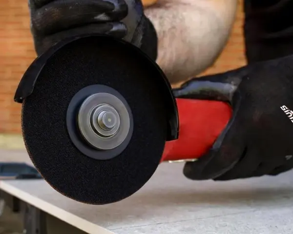 Mani guantate usano una smerigliatrice angolare per mostrare come tagliare le piastrelle con precisione.