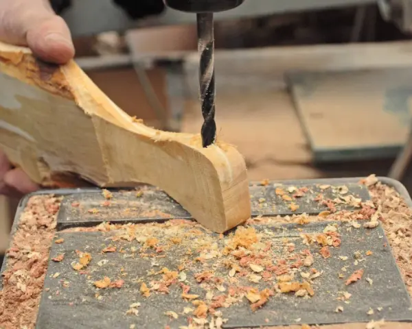 Mano che trapana un pezzo di legno grezzo, creando un tagliere legno fai da te. Segatura ovunque.