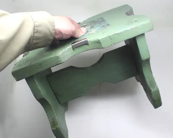 Mano che tiene uno sgabello di legno verde, pronto per verniciare con bomboletta spray.