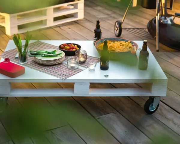 Tavolo con pallet fai da te, pronto per un barbecue con birre, patatine e pomodorini.