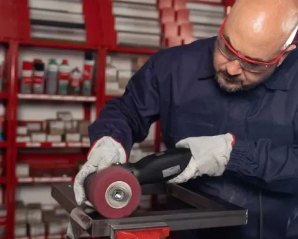 Operaio con occhiali protettivi e guanti lavora su un pezzo metallico, usando una smerigliatrice. Impara come saldare acciaio inox con precisione.