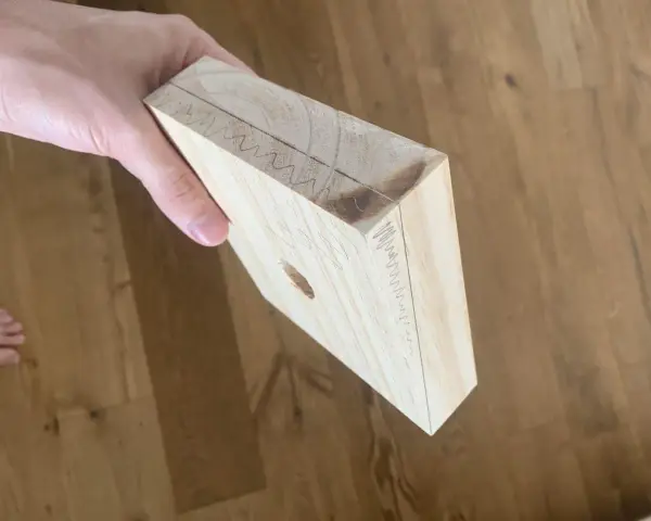 Mano che tiene un pezzo di legno con segni di matita, come se si stesse pensando a come tagliare il legno senza attrezzi.