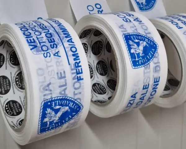Rotoli di nastri adesivi con scritte blu: "Veicolo Sottosequestro", "Polizia Stradale". Diversi tipi di nastri per imballaggi.