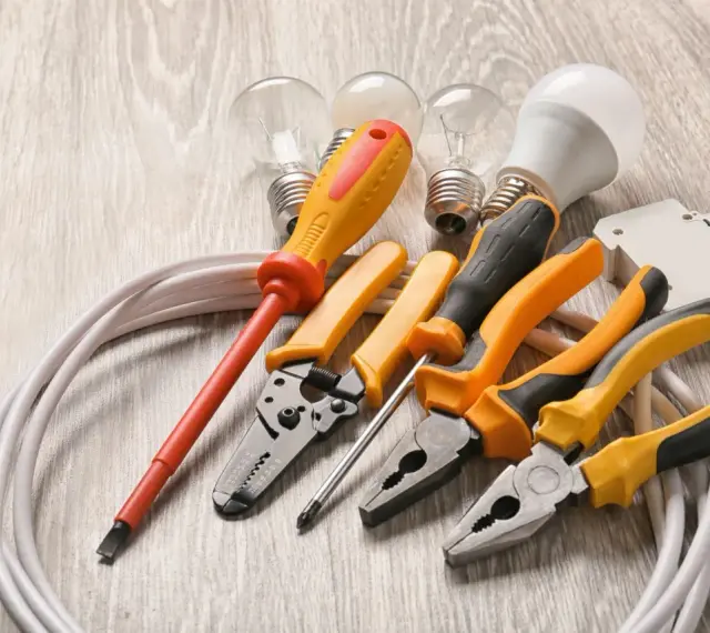Un set di strumenti per elettricisti: pinze, cacciaviti, lampadine e cavi su un tavolo di legno.