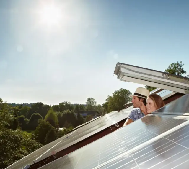 Coppia sorridente guarda il sole su un tetto con pannelli fotovoltaici, pensando alla tabella rendimento pannelli fotovoltaici.