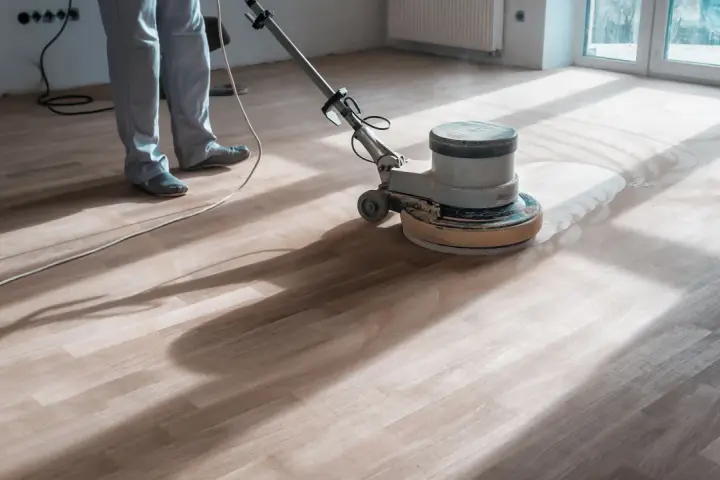 Un professionista usa una levigatrice per decerare il parquet, sollevando una nuvola di polvere.