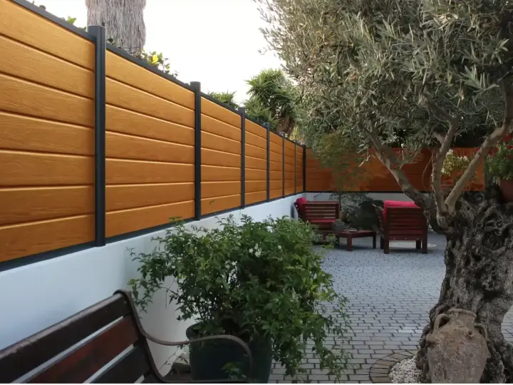 Pannello in legno effetto teak fissato a un muro bianco, con un ulivo secolare e arredi da esterno. Ideale per capire come fissare un pannello di legno al muro.