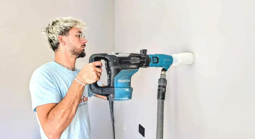 Giovane con capelli biondi usa un trapano Makita per fare un foro nel muro. Il trapano non buca muro, ma aspira la polvere.