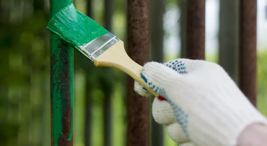 Mano guantata che vernicia di verde un palo di metallo arrugginito, rinnovando la verniciatura.