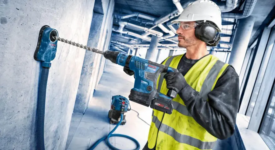 Operaio con trapano a percussione e punte trapano per cemento armato, pronto a forare un muro in cantiere.