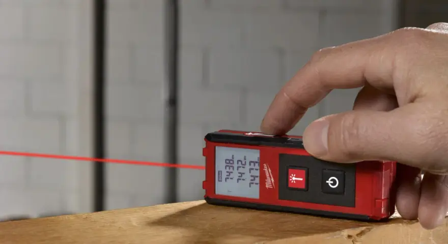 Dito come si usa il metro laser Milwaukee per misurazioni precise. Un dito preme il pulsante per attivare il raggio laser rosso.