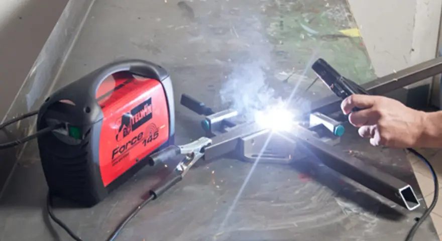 Saldare fili sottili con una saldatrice Telwin Force 145. Scintille luminose e fumo si alzano mentre un artigiano lavora.