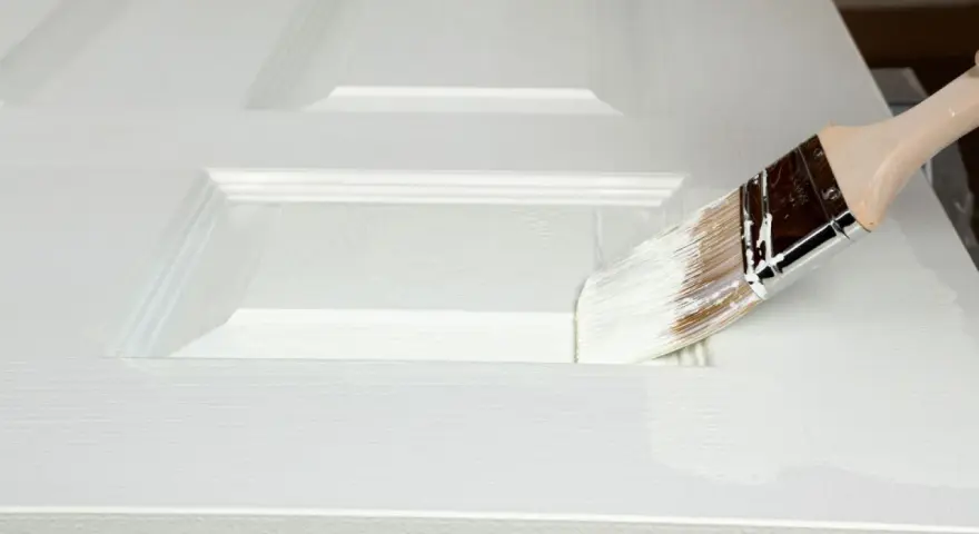 Pennello bianco applica vernice su porta in legno già verniciata, mostrando come verniciare una porta in legno già verniciata.